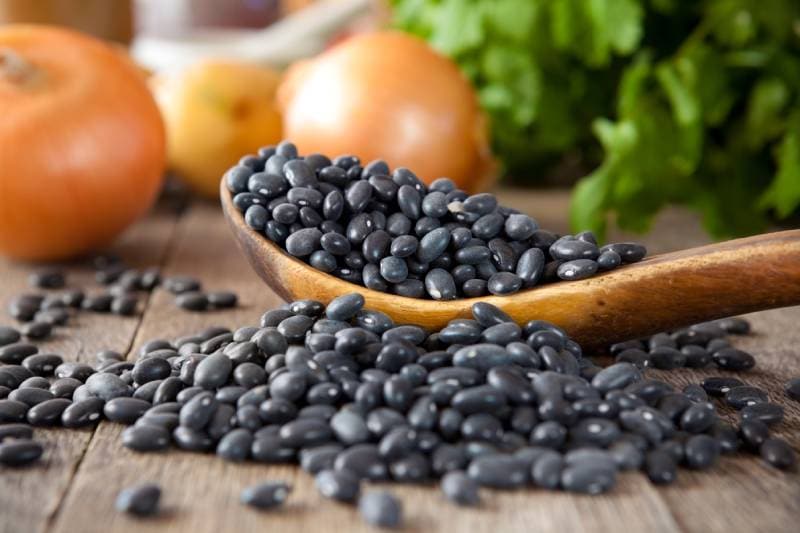 Black beans in a wooden spoon with cilantro and onions in the background