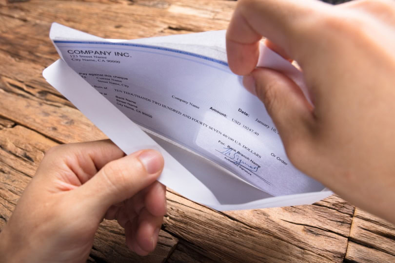 Hands holding a paycheck inside an envelope