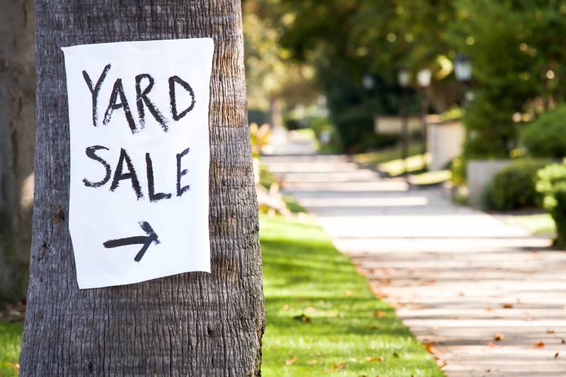 hand painted paper yard sale sign with direction arrow stapled to a palm tree