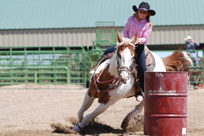 young cowgirl riding a beautiful paint horse in a barrel racing event