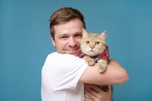 Caucasian young man with british tabby cat isolated on blue background